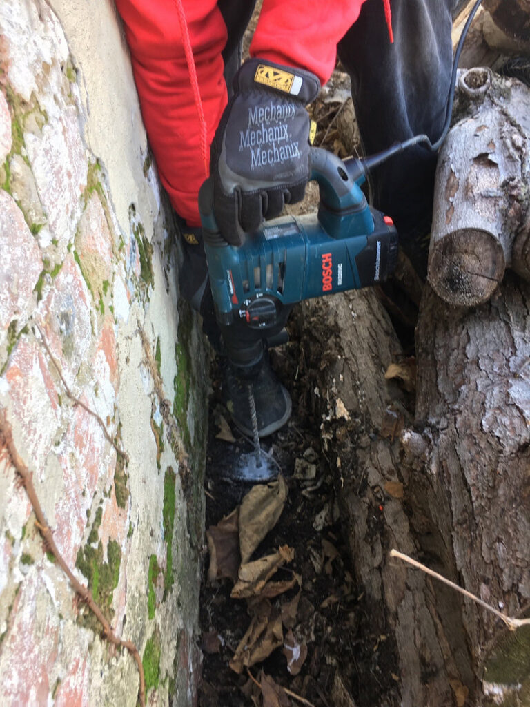 A pest control technician drilling into the ground for termite treatment by Genesis Termite and Pest Control in New Holland, PA.
