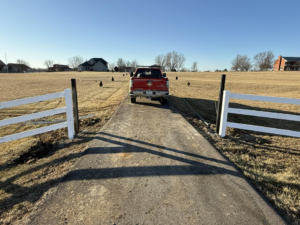 A driveway entrance with white fence posts installed, indicating a fencing project by Henderson Fence in Culpeper, VA.