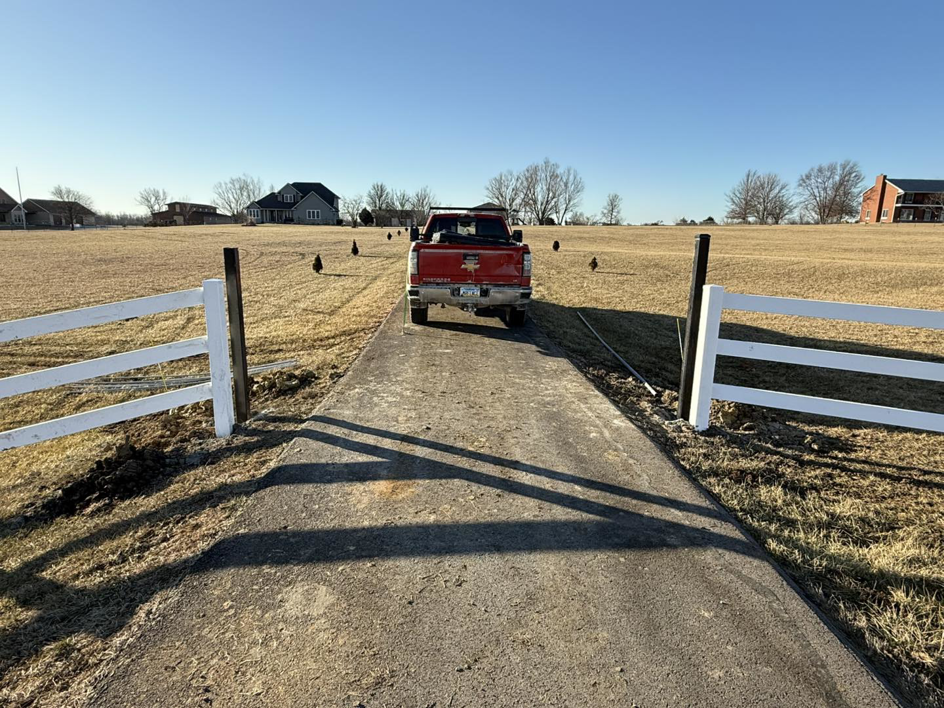 A driveway entrance with white fence posts installed, indicating a fencing project by Henderson Fence in Culpeper, VA.