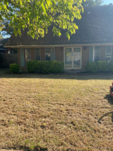 A dry, unkempt lawn with overgrown bushes in front of a house, ready for care from A&B Lawn Services in Baytown, TX.
