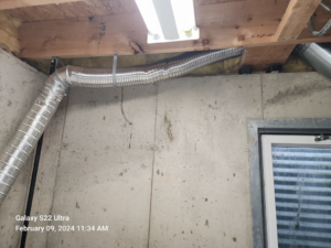 Flexible dryer vent ductwork installed along a concrete wall and wooden joists by Pro Power Air Duct & Dryer Vent Cleaning in Kenosha, WI.