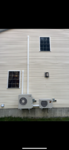 Two heat pump outdoor units installed on the yellow siding of a residential home by S&J Heat Pumps in Augusta, ME.