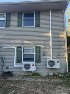 Two Mitsubishi heat pump outdoor units installed on the side of a residential building by S&J Heat Pumps in Augusta, ME.
