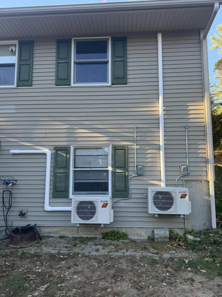 Two Mitsubishi heat pump outdoor units installed on the side of a residential building by S&J Heat Pumps in Augusta, ME.