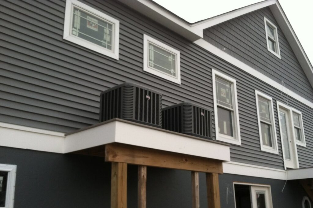 Two outdoor AC units installed on a raised platform next to a residential building by Tom's Heating & Air Conditioning LLC in Lacey Township, NJ.