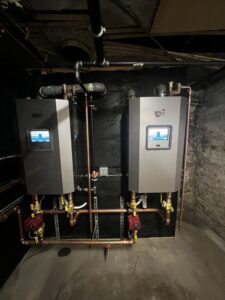 Two modern wall-mounted boilers with associated copper piping installed in a utility room by All Points HVAC in Worcester, MA.