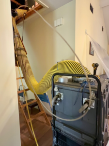 Air duct cleaning equipment with a large yellow hose extending from an attic to a powerful vacuum unit at Duct Doctor of Baton Rouge, LA.