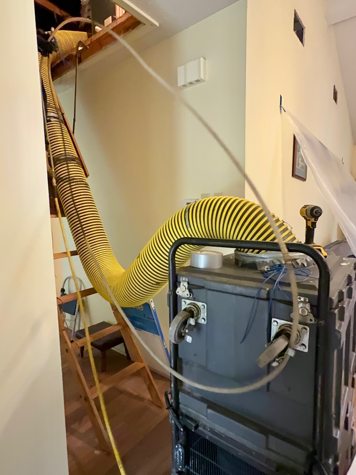 Air duct cleaning equipment with a large yellow hose extending from an attic to a powerful vacuum unit at Duct Doctor of Baton Rouge, LA.