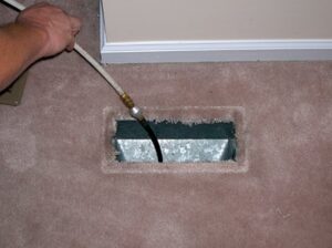 A hand performing duct cleaning service by inserting a tool into a carpeted floor vent, offered by The Right Flow Heating and Air LLC in Lawton, OK