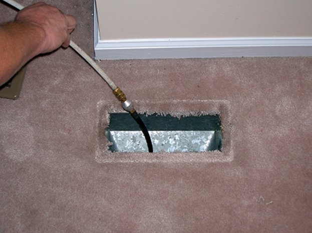 A hand performing duct cleaning service by inserting a tool into a carpeted floor vent, offered by The Right Flow Heating and Air LLC in Lawton, OK