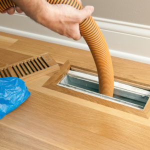 A technician performing duct cleaning service by inserting a hose into a floor vent at Total Comfort, Inc. in Danbury, CT