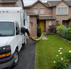 A professional duct cleaning service van with a large hose extending into a residential house by JJ Duct Cleaning in Aurora, IL
