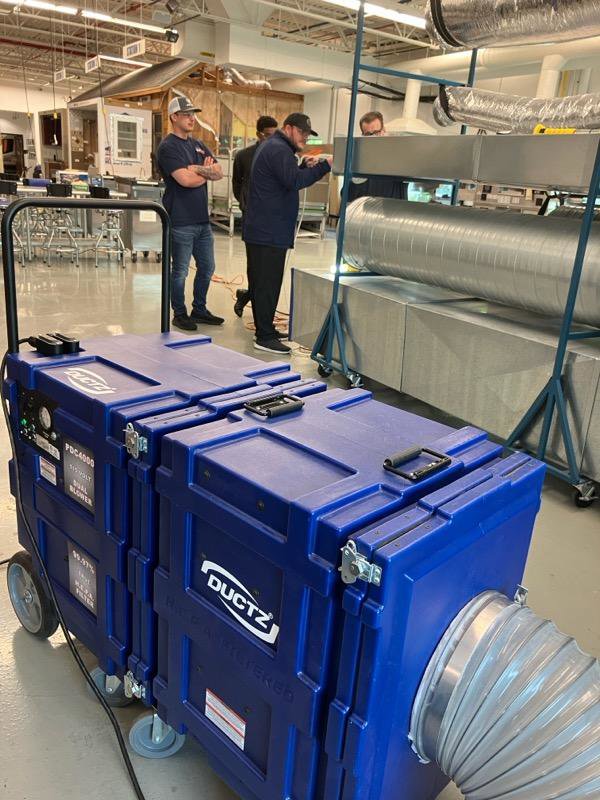 Large blue DUCTZ air purification machine in a workshop, with technicians working on duct systems at DUCTZ of Siouxland in Vermillion, SD.