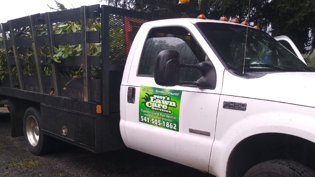 A white dump truck with Tony's Lawn Care Services decal, loaded with green waste for disposal in Greenville, SC.