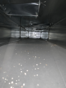 The dusty interior of a rectangular air duct, ready for professional cleaning by Air Duct Solutions in Waukee, IA.
