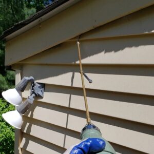 A pest control technician spraying the eaves of a house to treat for insects and pests by Serene Property Services LLC in Albany, NY