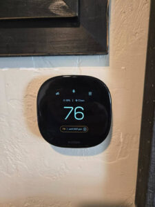 An Ecobee smart thermostat installed on a wall, showing temperature settings by Goodie Heating & Air in Sandy, UT.
