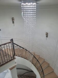 An elaborate, multi-tier chandelier hanging over a spiral staircase, installed by Warner Electric Service, LLC in Broken Arrow, OK.