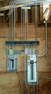 Two electrical breaker panels with conduits and wiring installed on a plywood wall by Ready Electric 24/7 in Knoxville, TN.