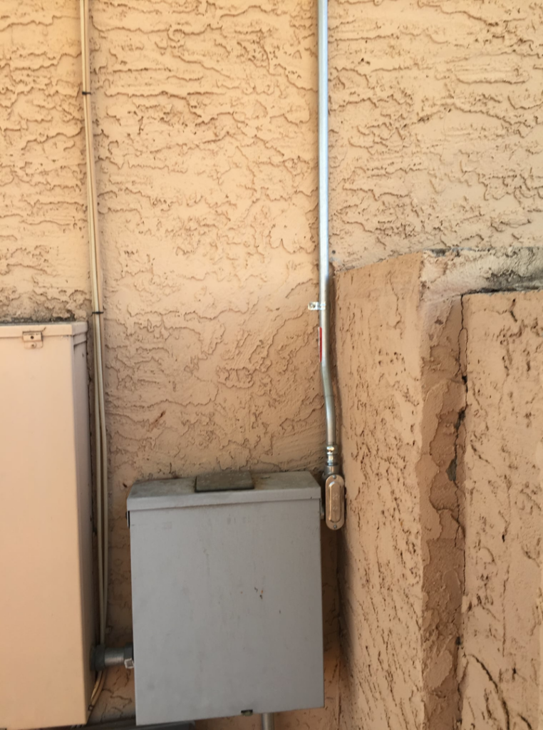 Newly installed electrical conduit and a service box on a building exterior by Earth Electric in Mesa, AZ