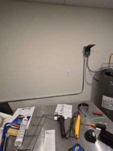 Electrical conduit and a disconnect box installed on a wall with tools on a workbench by DHJ Electric in Methuen, MA.