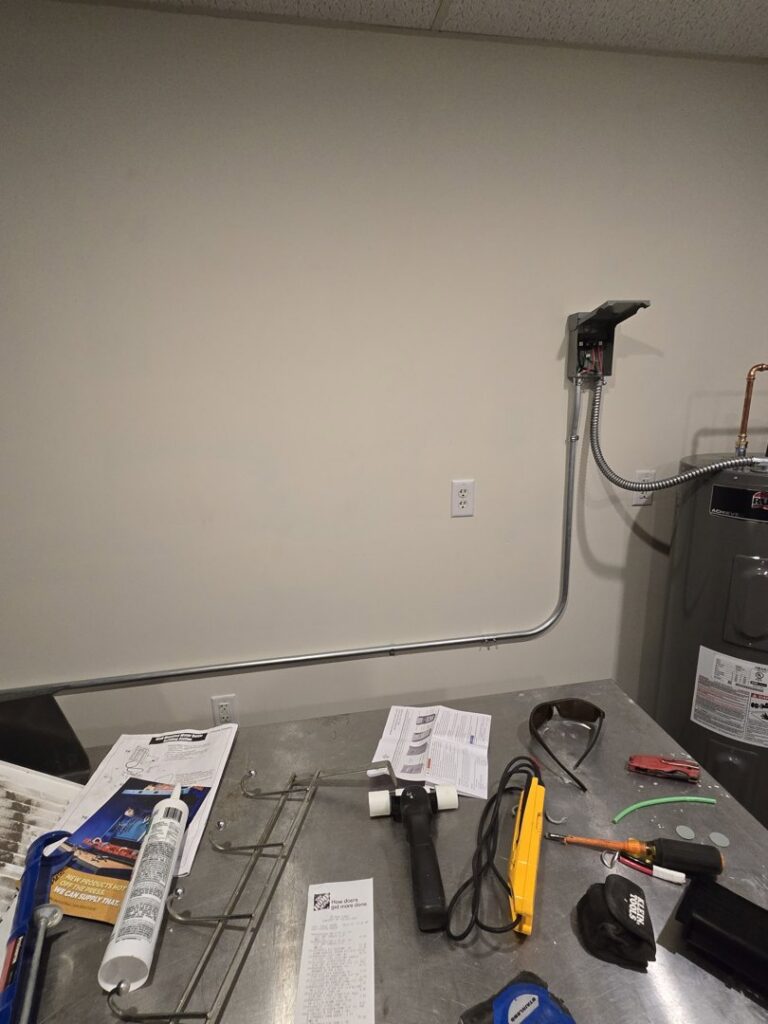 Electrical conduit and a disconnect box installed on a wall with tools on a workbench by DHJ Electric in Methuen, MA.