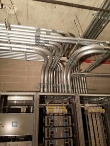 Multiple electrical conduits neatly installed along a ceiling and wall, connecting to electrical panels, by Bottom To The Top Electric LLC in Lakewood, CO.