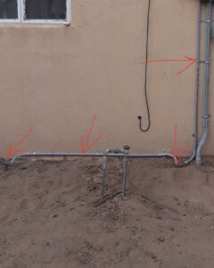 Exterior electrical conduit installation along a building wall and ground, indicating professional work by Certified Electrician Albuquerque NM.