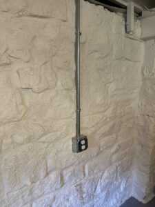 Electrical conduit and outlet installed on a white stone wall by Jeremy Electrical in Roeland Park, KS.