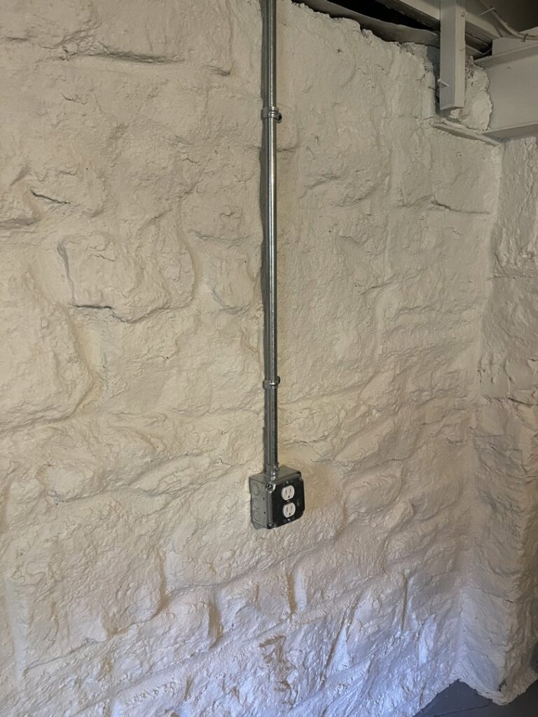 Electrical conduit and outlet installed on a white stone wall by Jeremy Electrical in Roeland Park, KS.