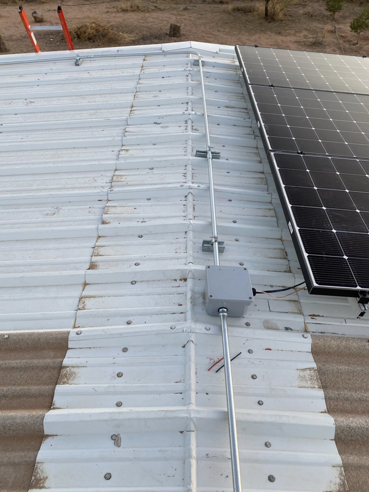 Electrical conduit and a junction box installed on a metal roof next to solar panels by Flores power solutions in El Paso, TX.