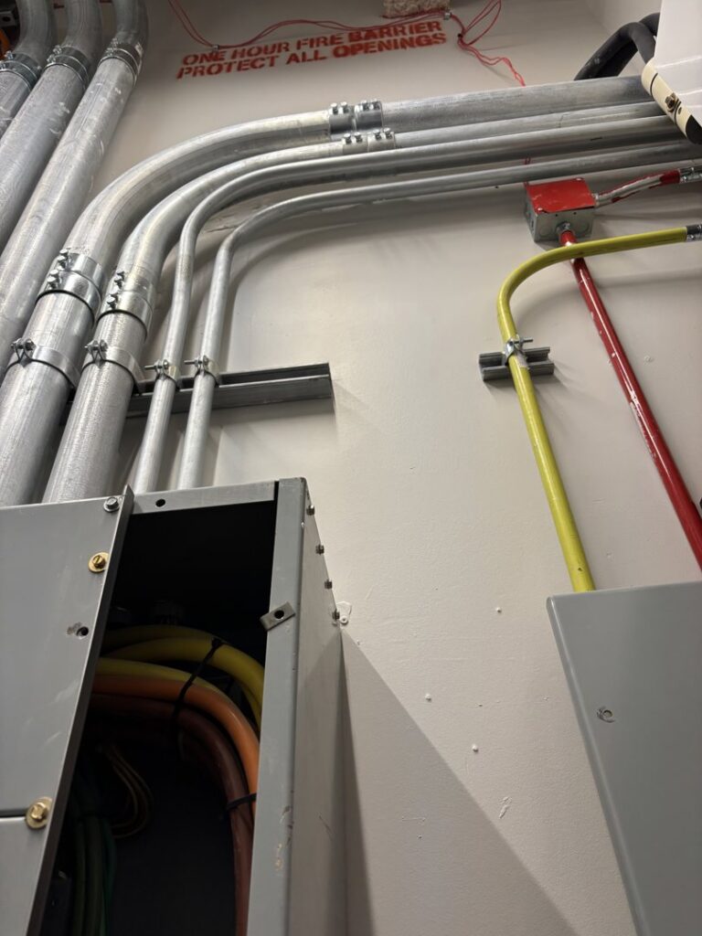 Electrical conduits and wiring installed along a wall with an open junction box by Tenax Electrical Company in Jacksonville, FL.