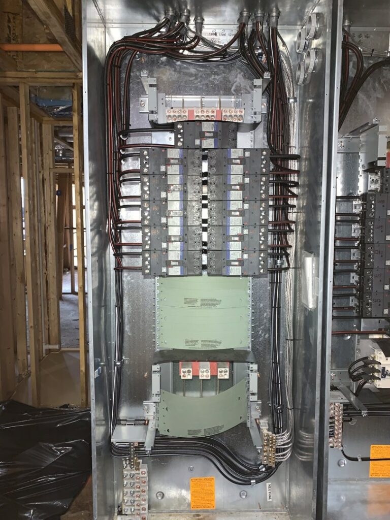 Large electrical distribution panel with multiple breakers and conduits in a new construction, installed by P&E Electric in Denver, CO.
