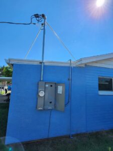 An electrical meter and an open service panel on the exterior of a blue building by CDB Electrical LLC in Tucson, AZ.