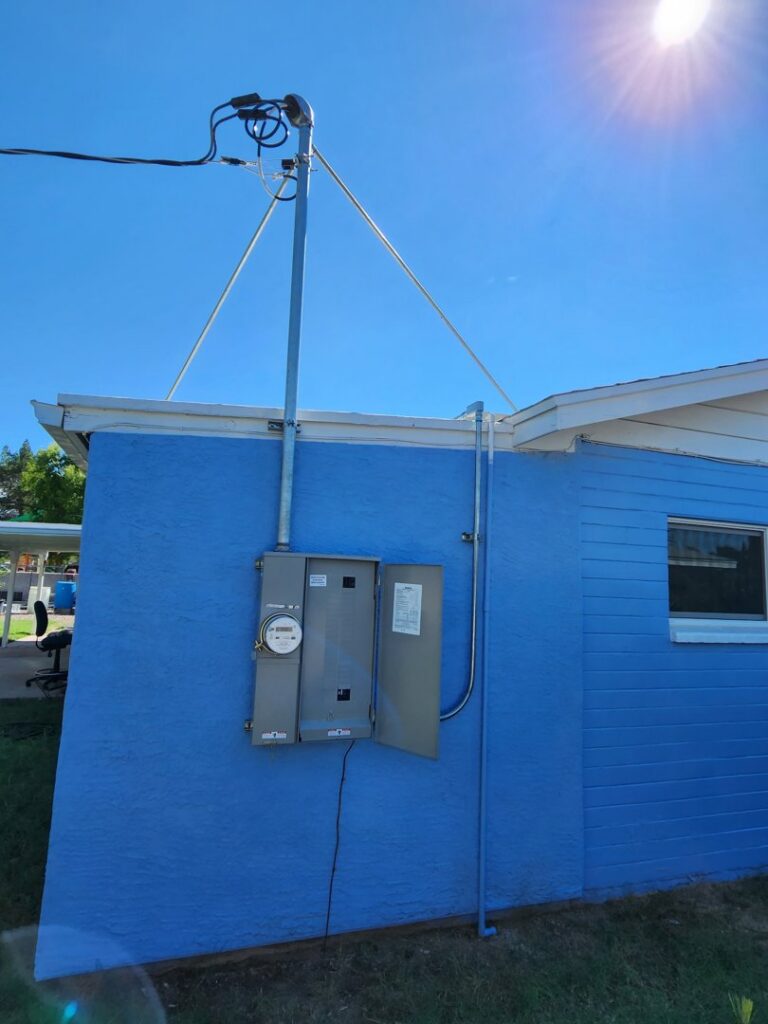 An electrical meter and an open service panel on the exterior of a blue building by CDB Electrical LLC in Tucson, AZ.