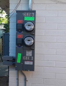 An outdoor electrical meter panel with two meters and emergency disconnects installed on a brick wall by Certified Electrician Albuquerque NM.