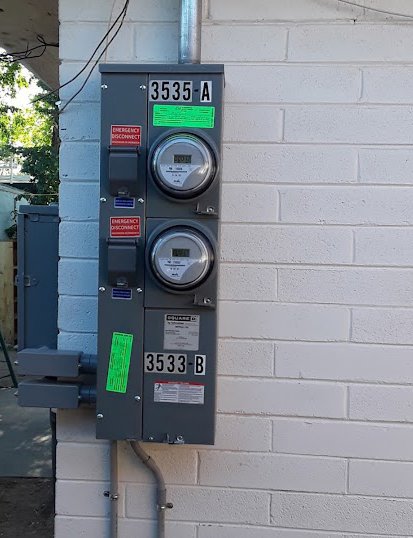An outdoor electrical meter panel with two meters and emergency disconnects installed on a brick wall by Certified Electrician Albuquerque NM.