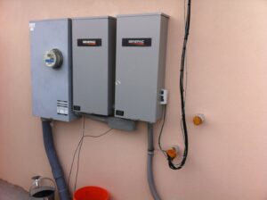 An electrical meter, transfer switch, and conduit installed on the side of a house by Generator Experts of Oklahoma in Norman, OK.