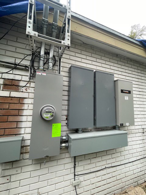Exterior view of multiple electrical meters, service panels, and a whole home generator installed by LOJ Electric, LLC in Houston, TX.