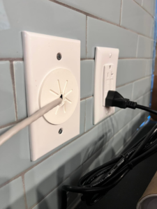 A modern electrical outlet and cable pass-through installed on a tiled wall by Solution Electric in Houston, TX.