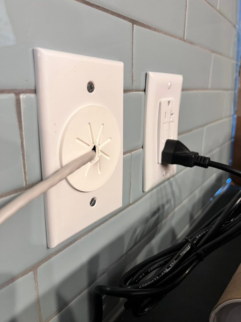 A modern electrical outlet and cable pass-through installed on a tiled wall by Solution Electric in Houston, TX.