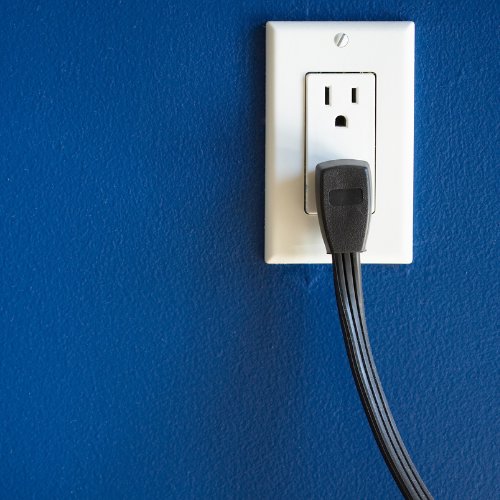 A properly installed electrical outlet with a plug on a blue wall, representing services by D. Geer Electric Inc. in Waukegan, IL.