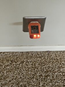 An electrician's outlet tester plugged into a wall outlet, showing indicator lights, by Powered Electrical & Lighting Services LLC in Springfield, MO.