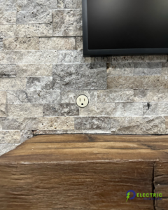 An electrical outlet installed in a stone wall below a television, completed by O Electric Services in Dallas, TX.