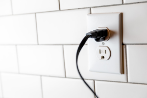 A standard electrical outlet with a black cord plugged in, installed by Jarvie Electric in Rochester, NY.