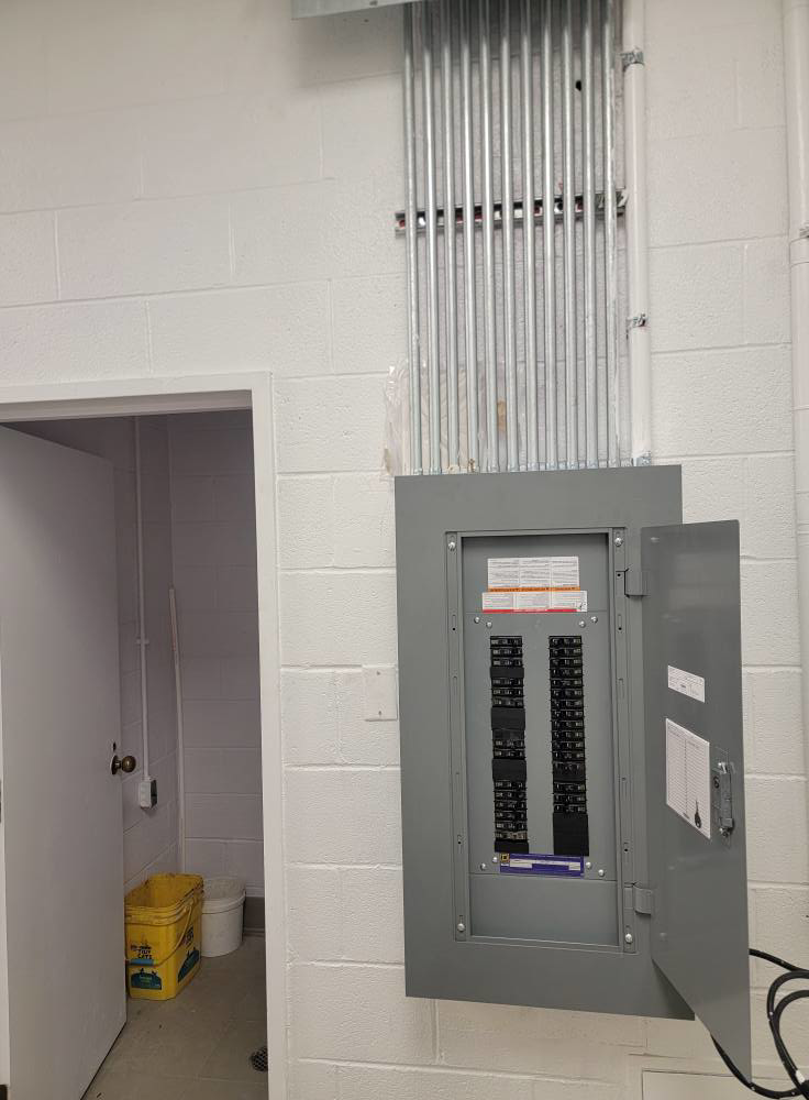 An open electrical panel with conduit wiring installed on a white brick wall by BESTA in Perkasie, PA.