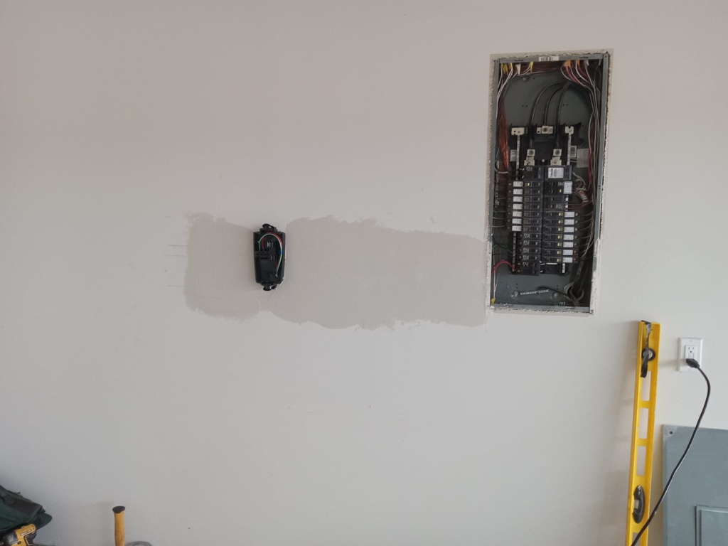 An electrical panel and new outlet being installed on a wall by Valle Home Maintenance in Houston, TX