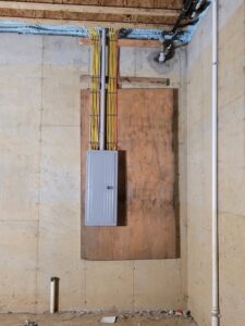An electrical panel with conduit and wiring installed in an unfinished basement, demonstrating work by New York Electrical Design in Freeport, NY