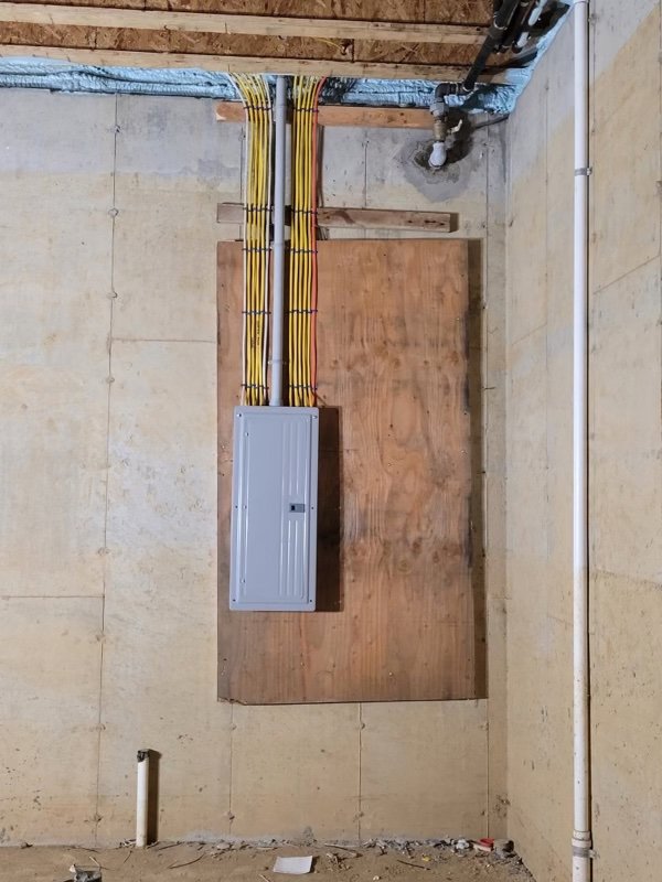 An electrical panel with conduit and wiring installed in an unfinished basement, demonstrating work by New York Electrical Design in Freeport, NY