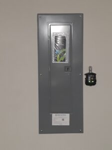An electrical panel with Crest Electrical Solutions branding and a small device plugged into an adjacent outlet in Arlington, TX.